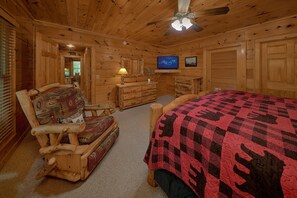 A log cabin bedroom with a bed, a chair, a dresser, a television, and a ceiling fan. - Hidden Escape | Hot Tub, Game Room, Fire Pit, Resort Pool, Fireplace + Free Attraction Tickets (Sevierville)