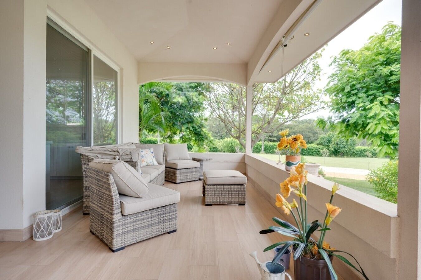 A spacious balcony with wicker furniture, a view of greenery, and a potted plant.