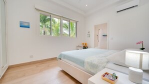 A modern bedroom with a large bed, a bedside table, a lamp, and a window with a view of greenery. - Beautiful home with pool in Rancho Cartagena! (Cartagena)
