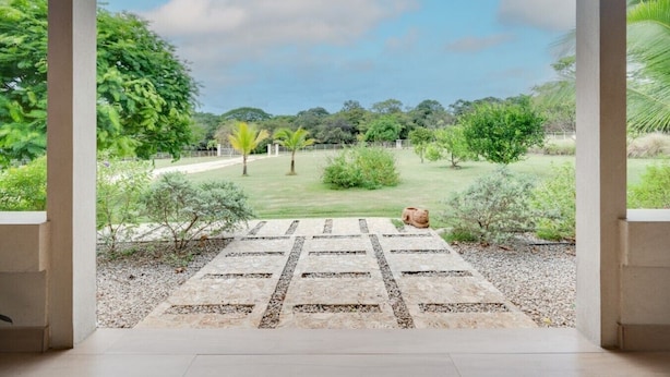 A view through a doorway into a garden with a paved area, a statue, and various plants. - Beautiful home with pool in Rancho Cartagena! (Cartagena)