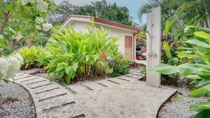 A garden pathway leading to a building with a tiled roof, surrounded by lush greenery and tropical plants. - Beautiful home with pool in Rancho Cartagena! (Cartagena)