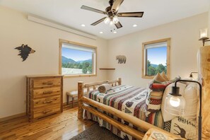 A bedroom with a wooden bed, a dresser, a ceiling fan, and two windows with mountain views. - 360 Mtn Views Close to Mt Princeton Hot Springs (Nathrop)
