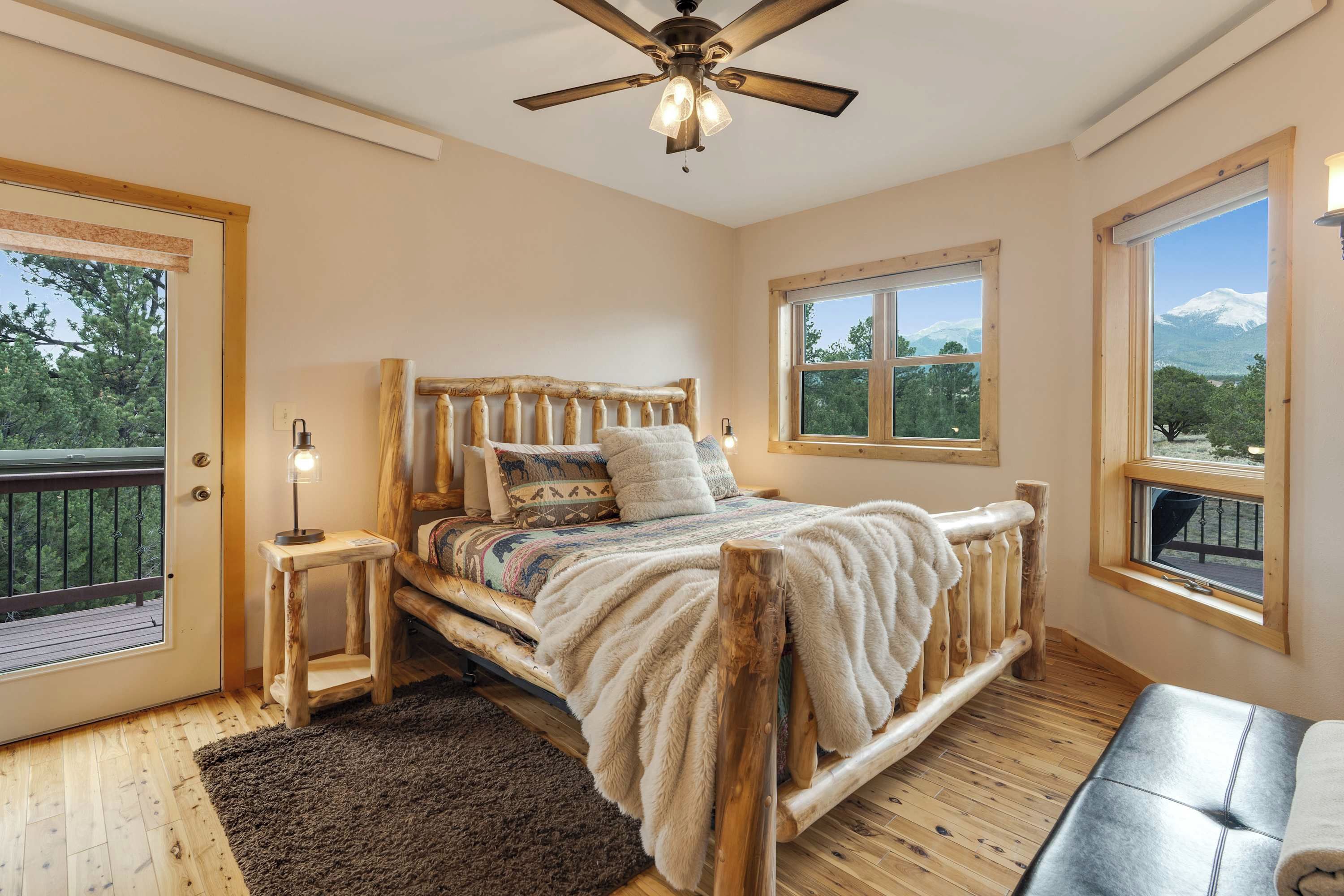 A bedroom with a wooden bed, a ceiling fan, a window with a view of a mountain, and a balcony with a railing. - 360 Mtn Views Close to Mt Princeton Hot Springs (Nathrop)