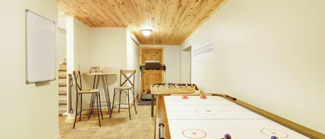 A room with a foosball table, two chairs, a small table with a box, and a whiteboard on the wall.