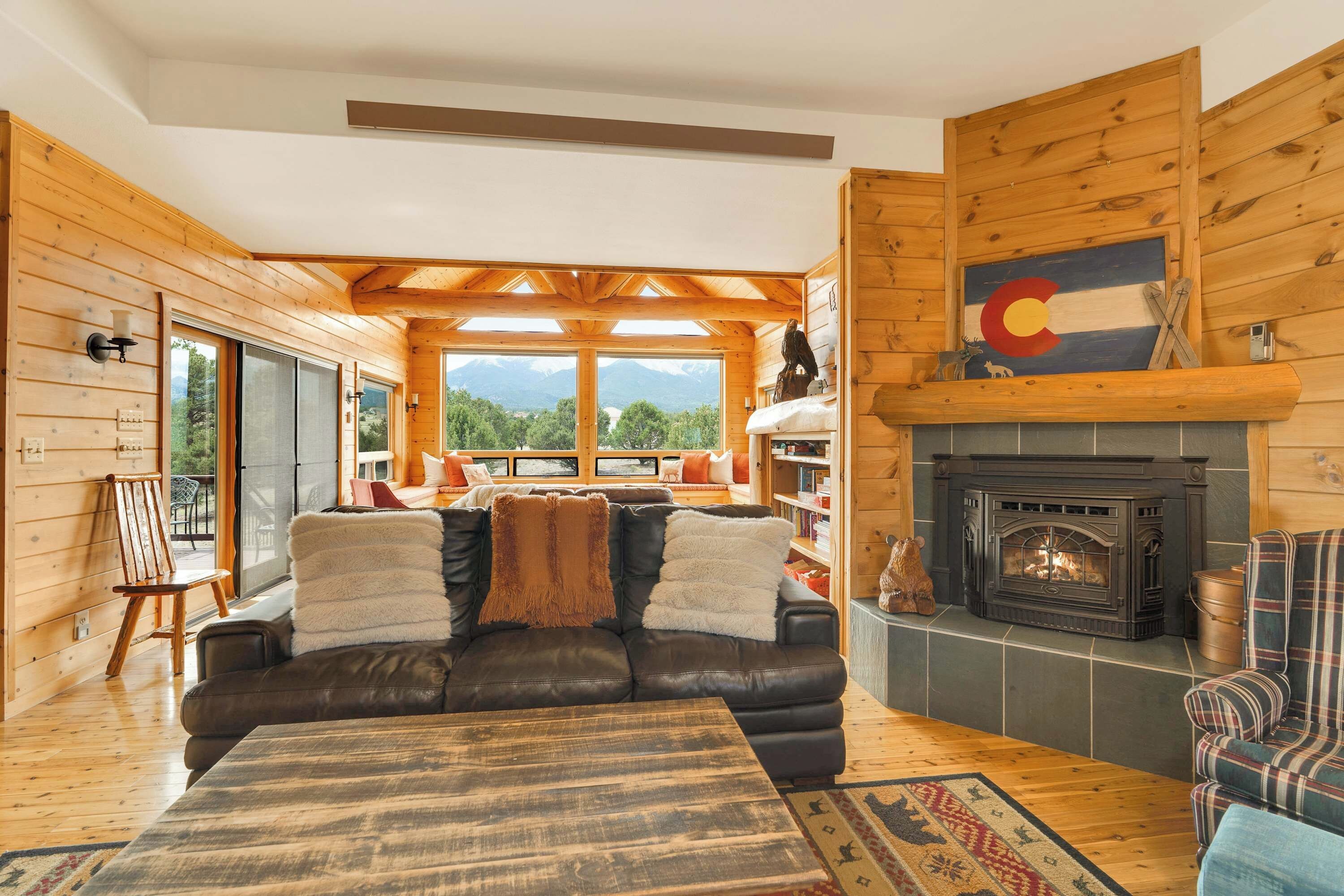 Interior acogedor de una cabaña con chimenea, un sofá de cuero y vistas a la montaña.