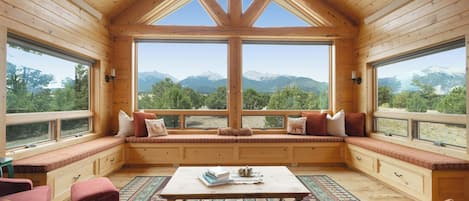 Interior acogedor de una cabaña con un amplio ventanal, paredes de madera y vistas a las montañas.