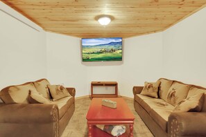 Un salon avec deux canapés en cuir marron, une table basse en bois et un téléviseur à écran plat fixé au mur, qui diffuse une image de paysage.