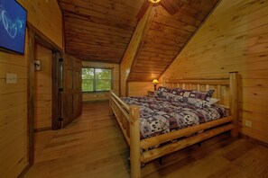 Een slaapkamer in een houten chalet, met een bed, nachtkastje, lamp en raam.