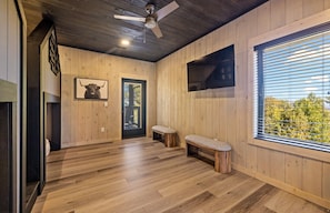 A wooden interior with a ceiling fan, a mounted TV, a framed picture, and a bench. - Ski Mountain Swim | Private Pool, Mtn Views, Hot Tub, Game Room, Sleeps 10 + Free Attraction Tickets (Gatlinburg)