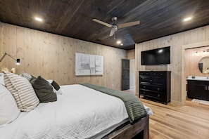 A bedroom with a bed, a ceiling fan, a flat-screen TV, a dresser, and a mirror. - Ski Mountain Swim | Private Pool, Mtn Views, Hot Tub, Game Room, Sleeps 10 + Free Attraction Tickets (Gatlinburg)