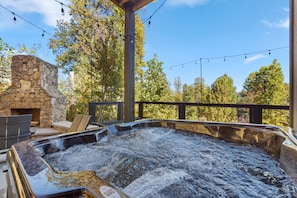 A hot tub with a stone fireplace and outdoor seating. - Ski Mountain Swim | Private Pool, Mtn Views, Hot Tub, Game Room, Sleeps 10 + Free Attraction Tickets (Gatlinburg)