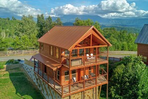 A multi-level wooden cabin with a balcony, surrounded by a fenced property and lush greenery. - Savannah Smiles Cabin Rental (Sevierville)