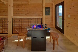 A wooden-floored room with a foosball table, two wooden stools, and a window with a view. - Savannah Smiles Cabin Rental (Sevierville)