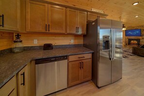 A kitchen with wooden cabinets, a stainless steel refrigerator, a built-in water dispenser, a toaster, and a dishwasher. - Savannah Smiles Cabin Rental (Sevierville)