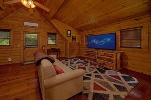 Ein gemütliches Blockhaus-Interieur mit einer Couch, einem Flachbildfernseher und einem gemusterten Teppich.
