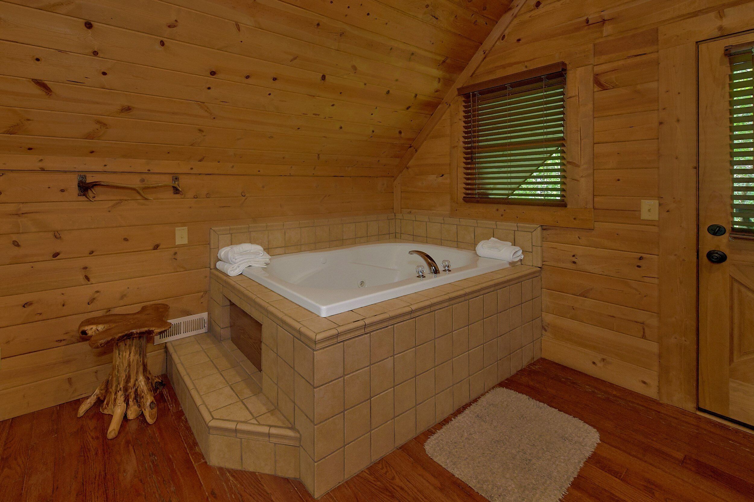 A wooden cabin with a bathroom featuring a bathtub, a towel rack, and a window with blinds.