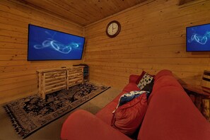 A cozy room with a red sofa, a wooden bench, a rug, and two large wall-mounted TVs displaying abstract images. - Hillside Dreams | Hot Tub, Game Room, Sleeps 10, Fire Pit, Fireplace + Free Attraction Tickets (Sevierville)