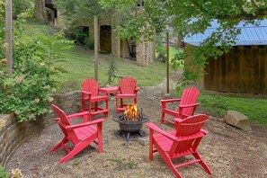 Ein Feuerkorb mit roten Adirondack-Stühlen, die ihn umgeben, in einem Garten.