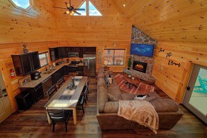 A cozy cabin interior with a kitchen, dining area, and a fireplace. - Livin' the Dream | Private Pool, Hot Tub, Game Room, Sleeps 12, Fireplace + Free Attraction Tickets (Pigeon Forge)