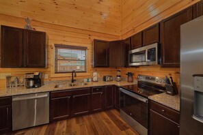 A modern kitchen with wooden cabinets, stainless steel appliances, and a granite countertop. - Livin' the Dream | Private Pool, Hot Tub, Game Room, Sleeps 12, Fireplace + Free Attraction Tickets (Pigeon Forge)