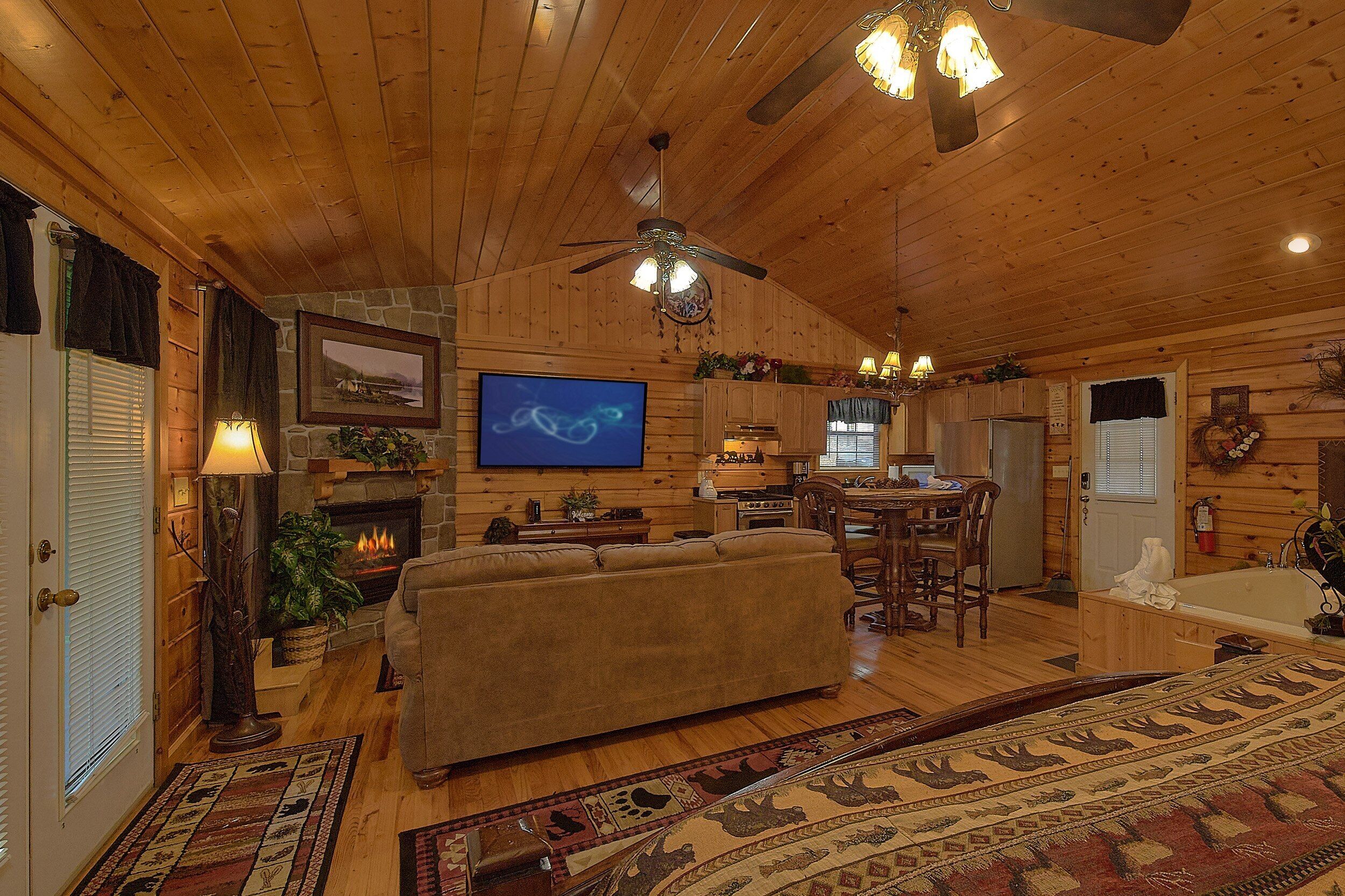 L’intérieur chaleureux d’un chalet avec une cheminée, un téléviseur, un plancher en bois et un ventilateur de plafond.