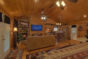 A cozy cabin interior with a fireplace, a television, wooden floors, and a ceiling fan. - Cherokee Nights Cabin Rental (Sevierville)