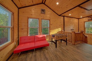 A cozy room with wooden walls, a red sofa, a foosball table, and large windows. - Relax II | Hot Tub, Game Room + Free Attraction Tickets (Sevierville)