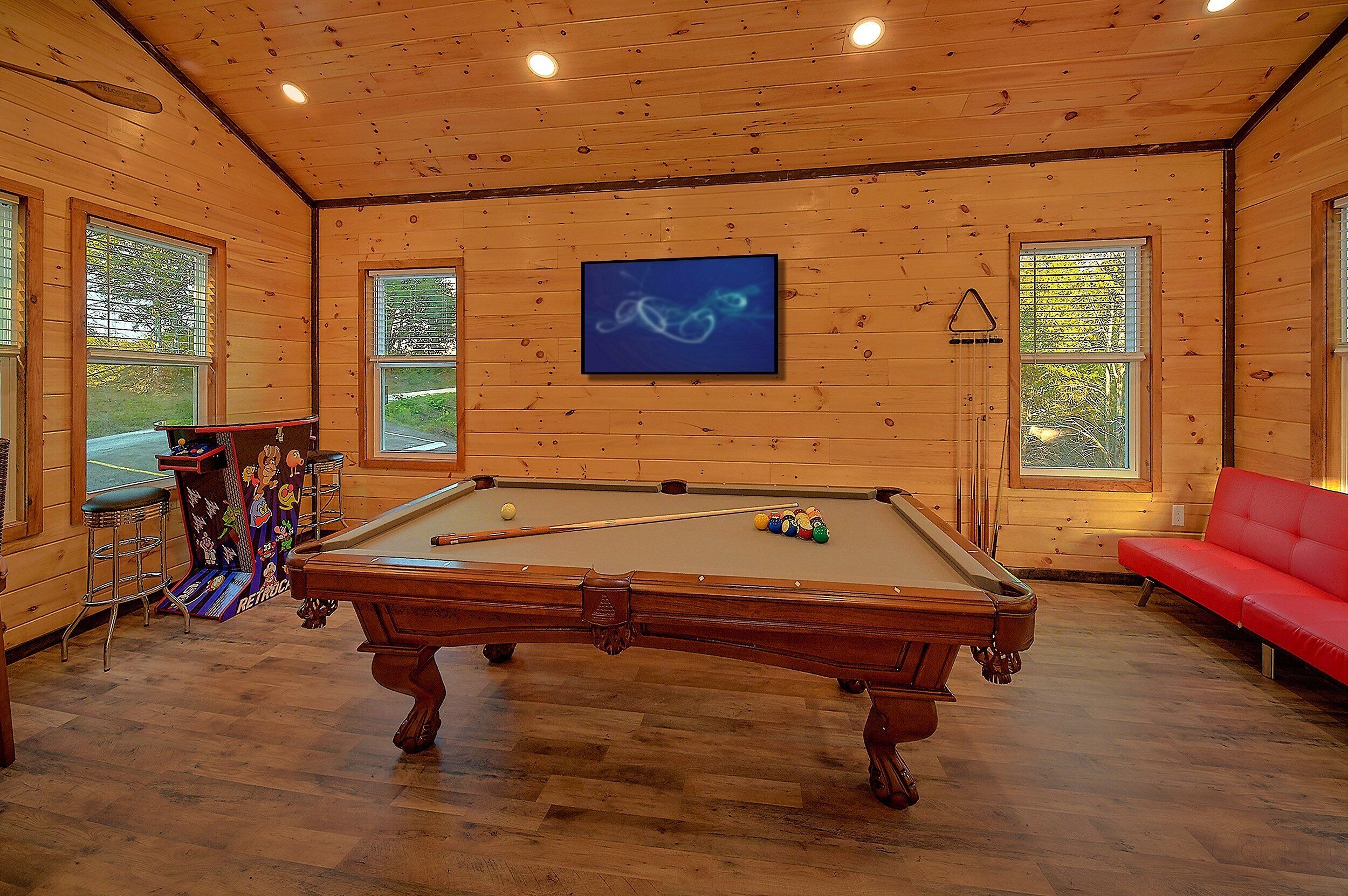 A pool table in a room with wooden walls and large windows.