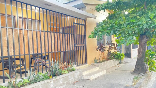 Zona residencial con entrada protegida, un sendero de hormigón y un árbol.