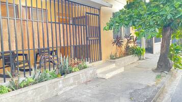 Zona residencial con entrada protegida, un sendero de hormigón y un árbol.