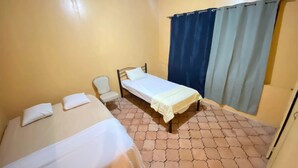 Una habitación con dos camas, una silla y un ventanal con cortinas.