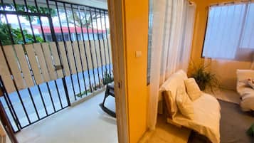 A room with a bed, a window with curtains, a door leading outside, and a view of a street with a parked car.