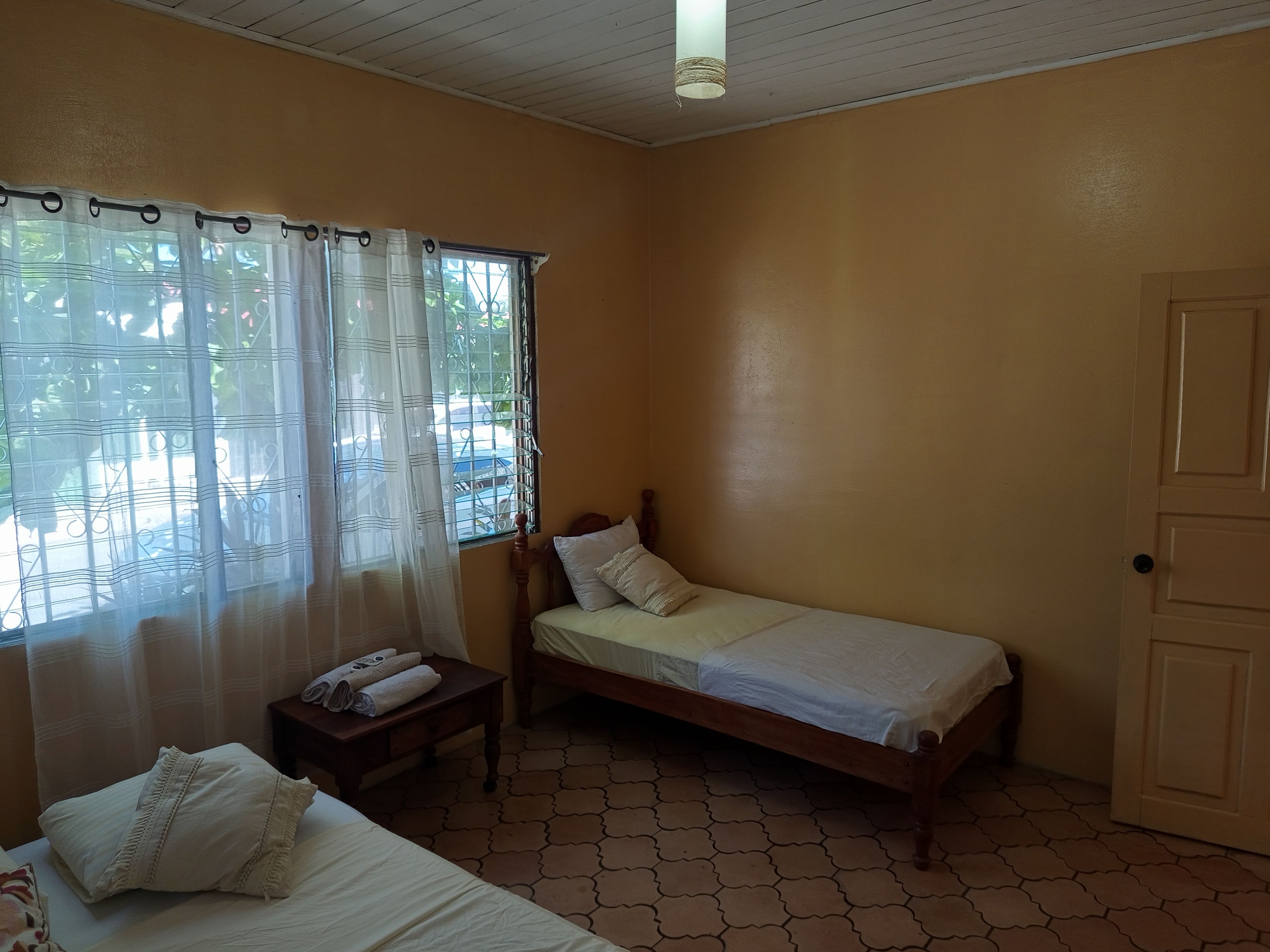 Una cama individual con estructura de madera, una mesita de noche con lámpara y una ventana con cortinas.