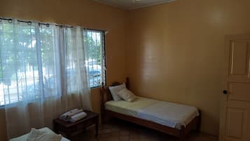 Una cama individual con estructura de madera, una mesita de noche con lámpara y una ventana con cortinas.
