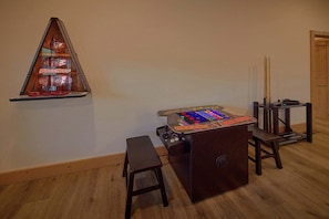 Une pièce avec un plancher en bois, une petite table sur laquelle est posé un jeu, une étagère fixée au mur avec un objet décoratif, et une porte.