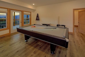 A pool table with balls and cues, wooden flooring, and a view through a glass door. - Sunrise Mountain Vista | Smoky Mtn Views, Hot Tub, Game Room, King Suites + Free Attraction Tickets (Gatlinburg)