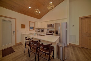 A modern kitchen with a central island, wooden chairs, a stainless steel refrigerator, and a microwave. - Sunrise Mountain Vista | Smoky Mtn Views, Hot Tub, Game Room, King Suites + Free Attraction Tickets (Gatlinburg)