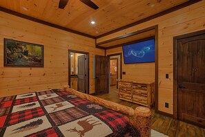 A log cabin interior with a large bed, a television, and a painting of bears. - Cubbs Dream Paradise | Private Pool, Theater, Smoky Mtn Views, Hot Tub + Free Attraction Tickets (Sevierville)
