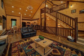 A spacious wooden interior with a black leather sofa, a wooden coffee table, and a staircase. - Cubbs Dream Paradise | Private Pool, Theater, Smoky Mtn Views, Hot Tub + Free Attraction Tickets (Sevierville)
