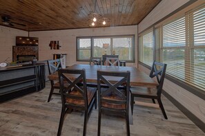 A dining area with a wooden table, dark chairs, and a view through large windows. - Top Notch Cabin Rental (Pigeon Forge)