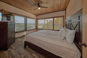 A bedroom with a bed, dresser, and windows. - Top Notch Cabin Rental (Pigeon Forge)