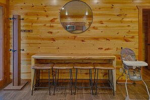 Ein Holzinterieur mit Barbereich, Hockern, einer Mikrowelle und einem Hochstuhl.