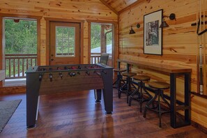 Une pièce au plancher de bois, avec un baby-foot, des tabourets de bar et un tableau encadré accroché au mur.