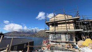 A building under construction with a mountain backdrop. - Lakehouse 63 – Brand- New Lakefront Villa with Spa (Queenstown)