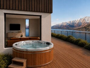 Ein modernes, Outdoor-Whirlbad mit Holzverkleidung, eine Sitzecke mit Sofa und Fernseher sowie ein malerischer Bergblick.