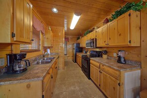 A wooden cabin interior with a kitchen featuring granite countertops, stainless steel appliances, and wooden cabinets. - A Glimpse of Heaven | Sweeping Mountain Views | Hot Tub (Sevierville)