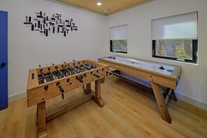 A room with a foosball table, a shuffleboard table, and a wall art installation. - Downtown Gatlinburg Cabin | Hot Tub, Near Downtown Gatlinburg, Game Room + Free Attraction Tickets (Gatlinburg)