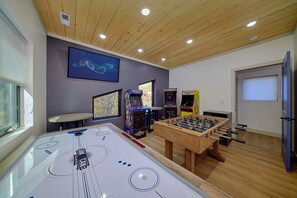 A room with a foosball table, arcade games, and a large TV screen. - Downtown Gatlinburg Cabin | Hot Tub, Near Downtown Gatlinburg, Game Room + Free Attraction Tickets (Gatlinburg)