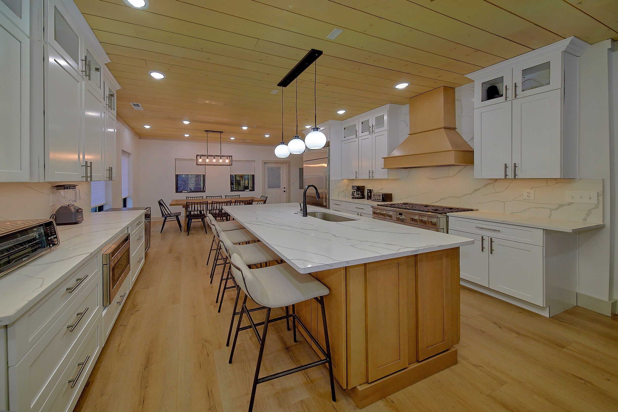 Une cuisine moderne avec des meubles blancs, un grand îlot central doté de tabourets et un autre îlot central intégrant une plaque de cuisson.