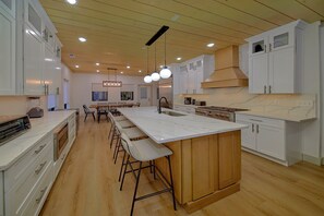 A modern kitchen with white cabinetry, a large island with bar stools, and a central island with a built-in stove. - Downtown Gatlinburg Cabin | Hot Tub, Near Downtown Gatlinburg, Game Room + Free Attraction Tickets (Gatlinburg)